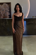 Woman in a brown evening gown standing indoors with a decorative wall in the background